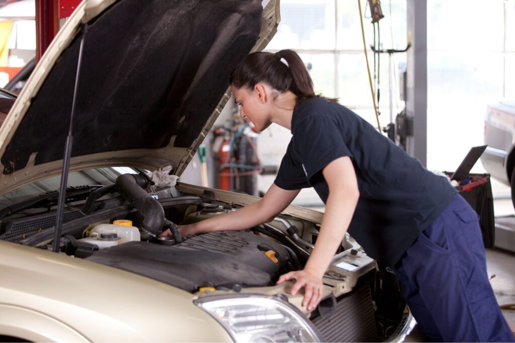 fille salariée du garage aspire qui regarde le moteur d'une voiture